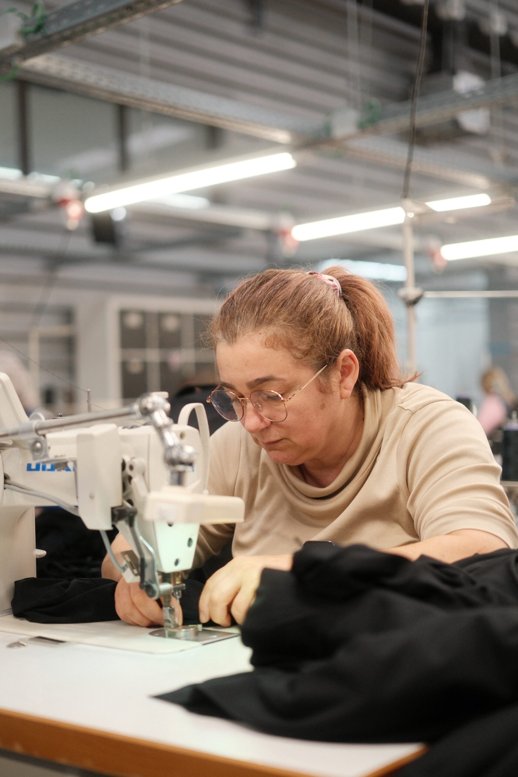 Ompelija ompelemassa teollisuusompelikoneen ääressä mustaa vaatetta Black Moda Portugalin tehtaalla. 